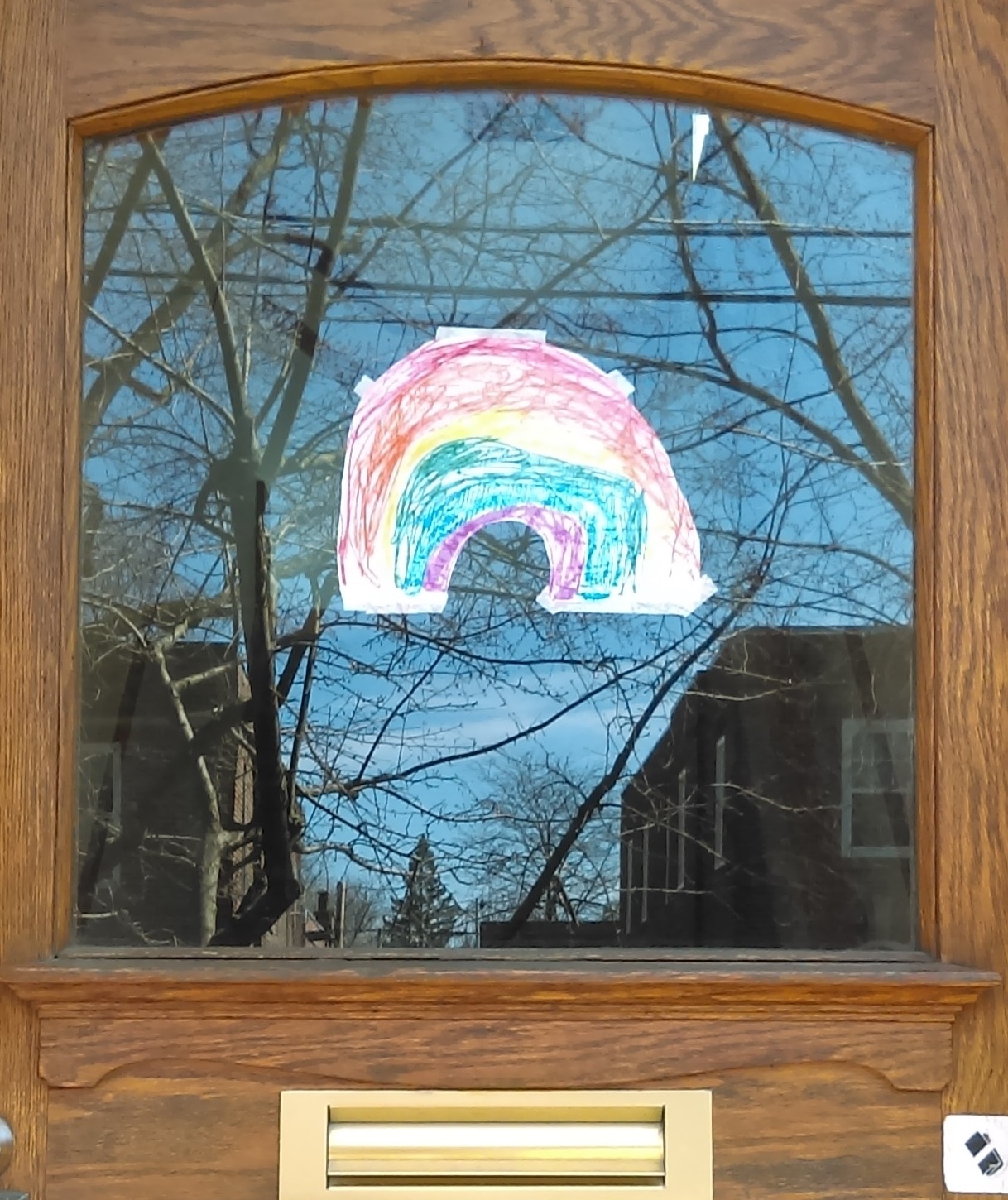a wooden door with a window. on the window is taped a rainbow drawn in crayon