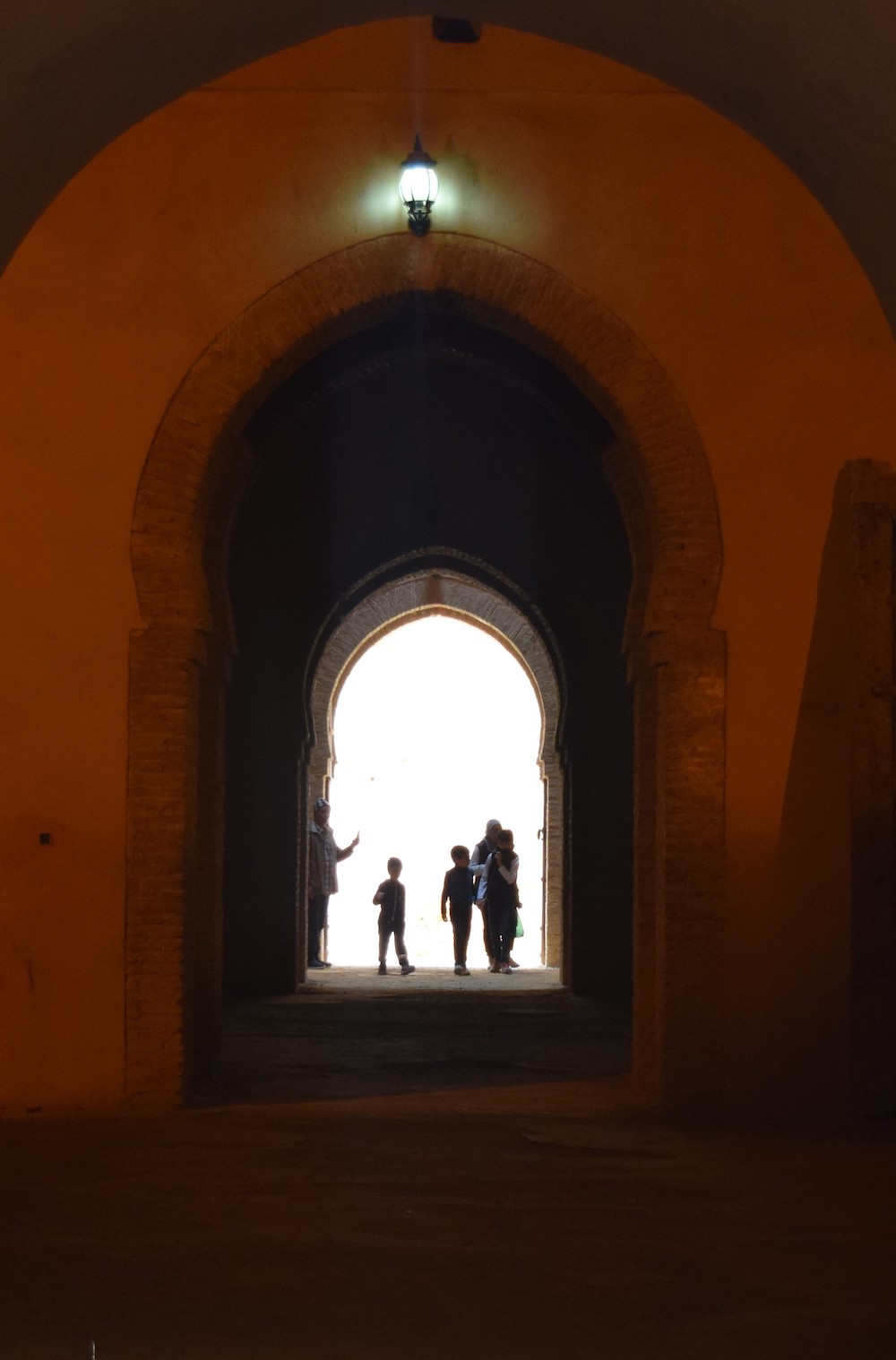 an arched doorway in Morocco with children's silhouettes lit up at the end of the hallway