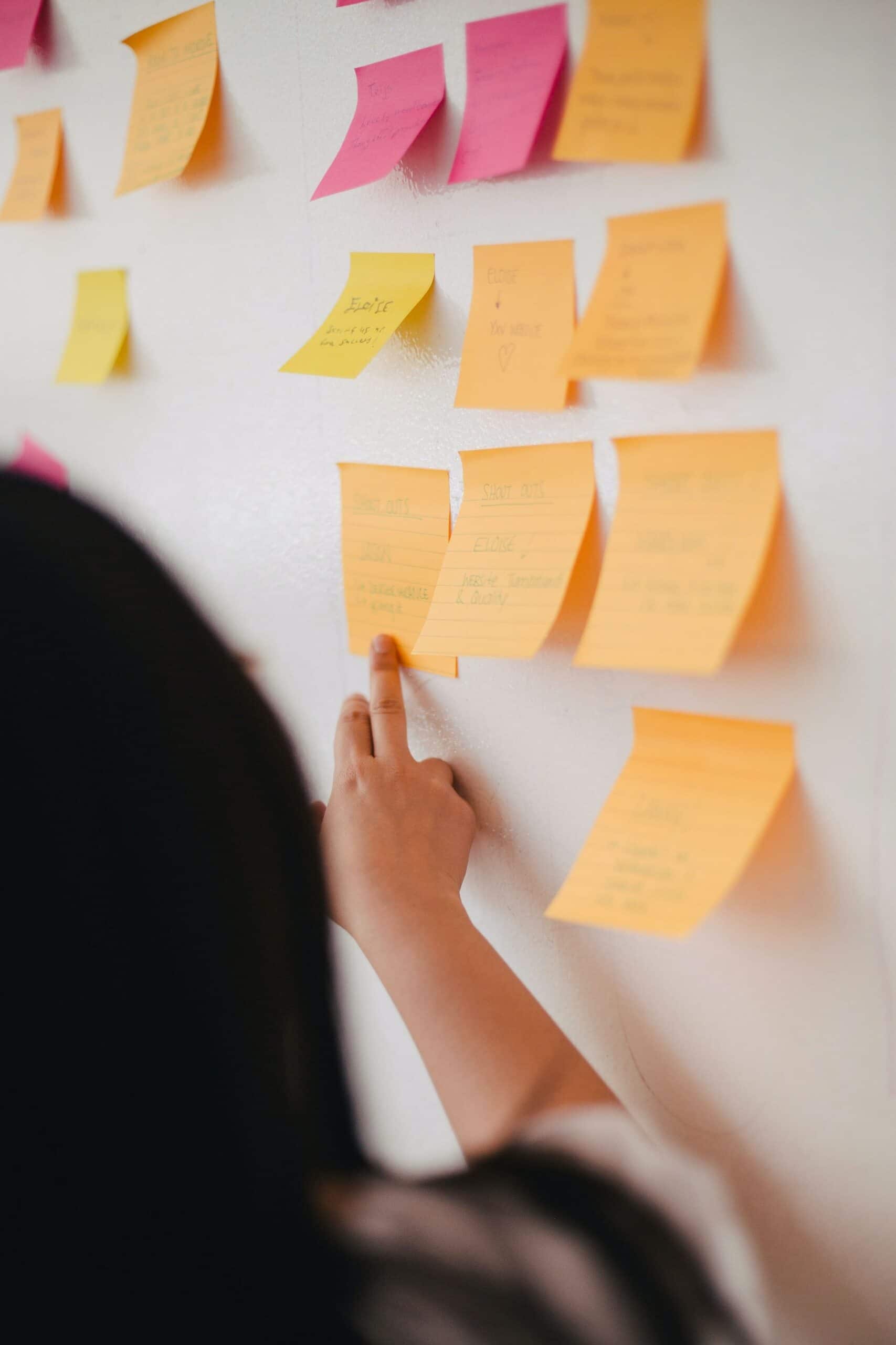 a woman points at a wall of post-it notes