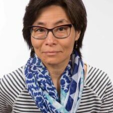 Su-Ming Khoo smiling in glasses with a blue scarf and striped shirt
